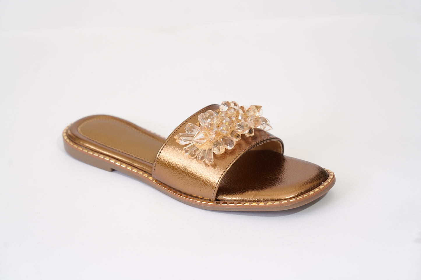 Side profile of Copper Mirage flat slider by Solemates by Palak — copper metallic pebbled upper with 3D crystal floral embellishment and gold stud sole trim, white background