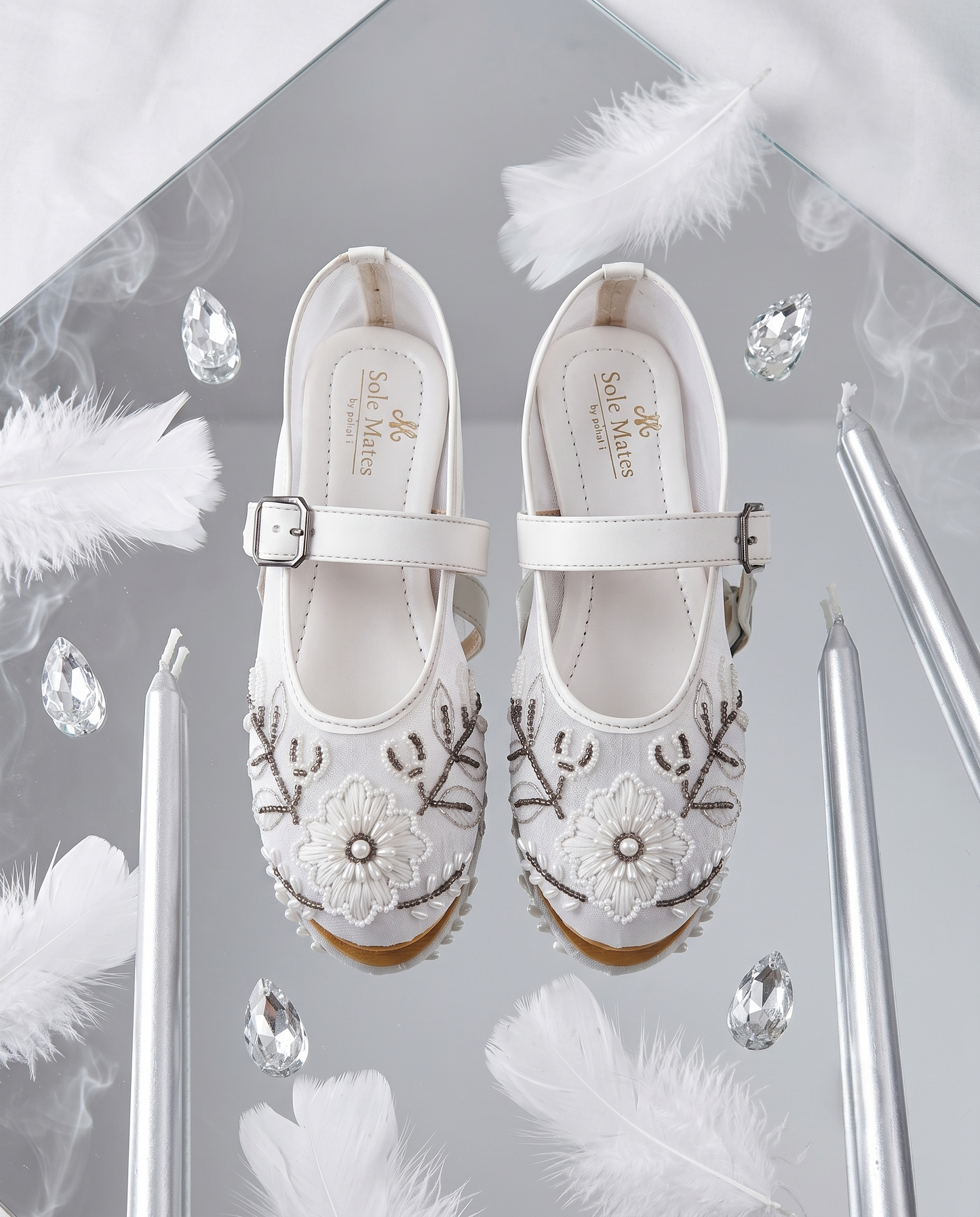 The Ballet Bloom Mary Janes flat lay on mirror with feathers and crystals — white pearl and bead embellished floral shimmer Mary Jane ballerinas by Solemates by Palak