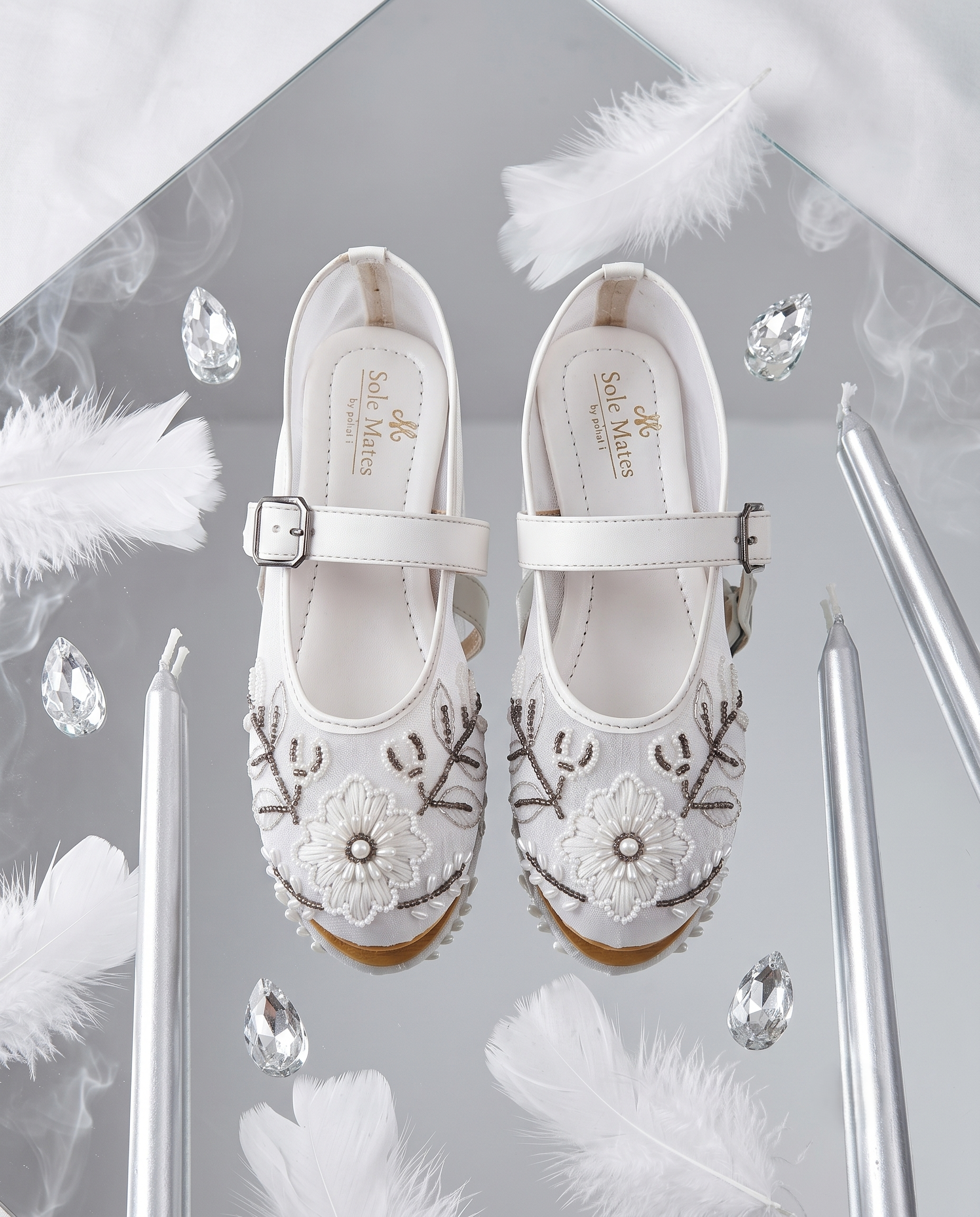 The Ballet Bloom Mary Janes flat lay on mirror with feathers and crystals — white pearl and bead embellished floral shimmer Mary Jane ballerinas by Solemates by Palak