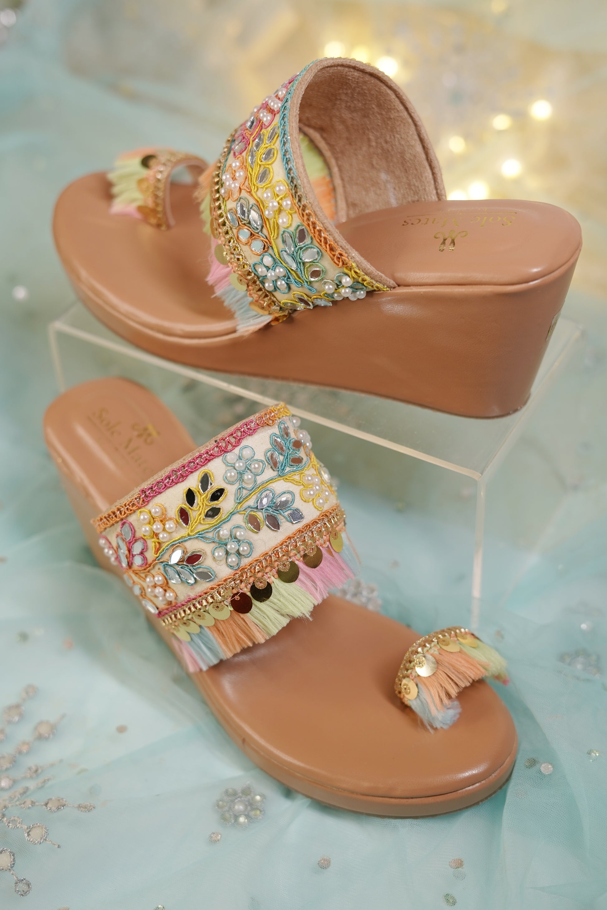 Gypsey Kohla Heels pair by Solemates by Palak on display stand — tan wedge sole with wide multicolour embroidered strap, mirror work, pearls, coin tassel danglers and kolhapuri toe ring strap